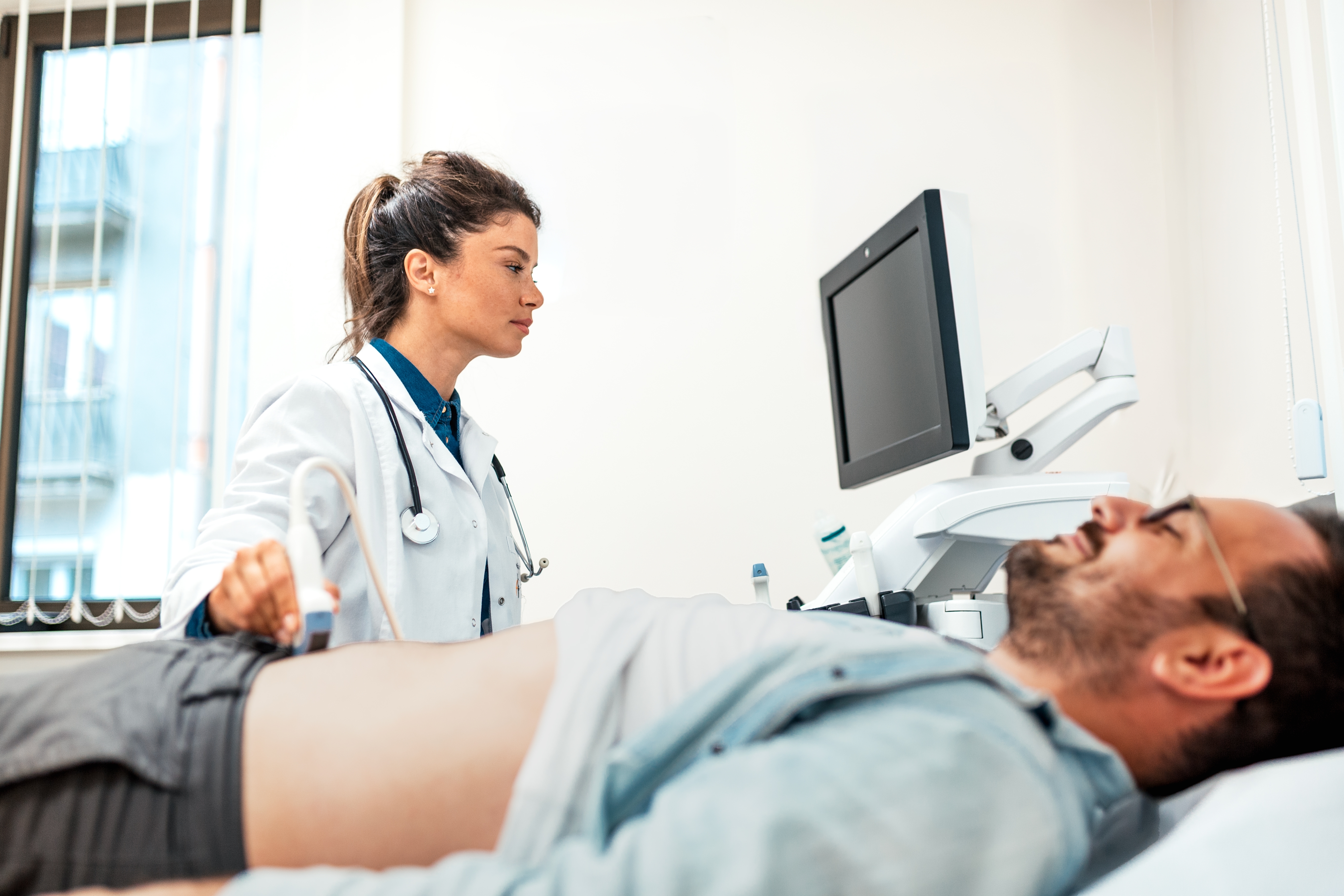 Ärztin, die bei männlichen Patienten eine Ultraschall-Untersuchung des Bauches durchführt.