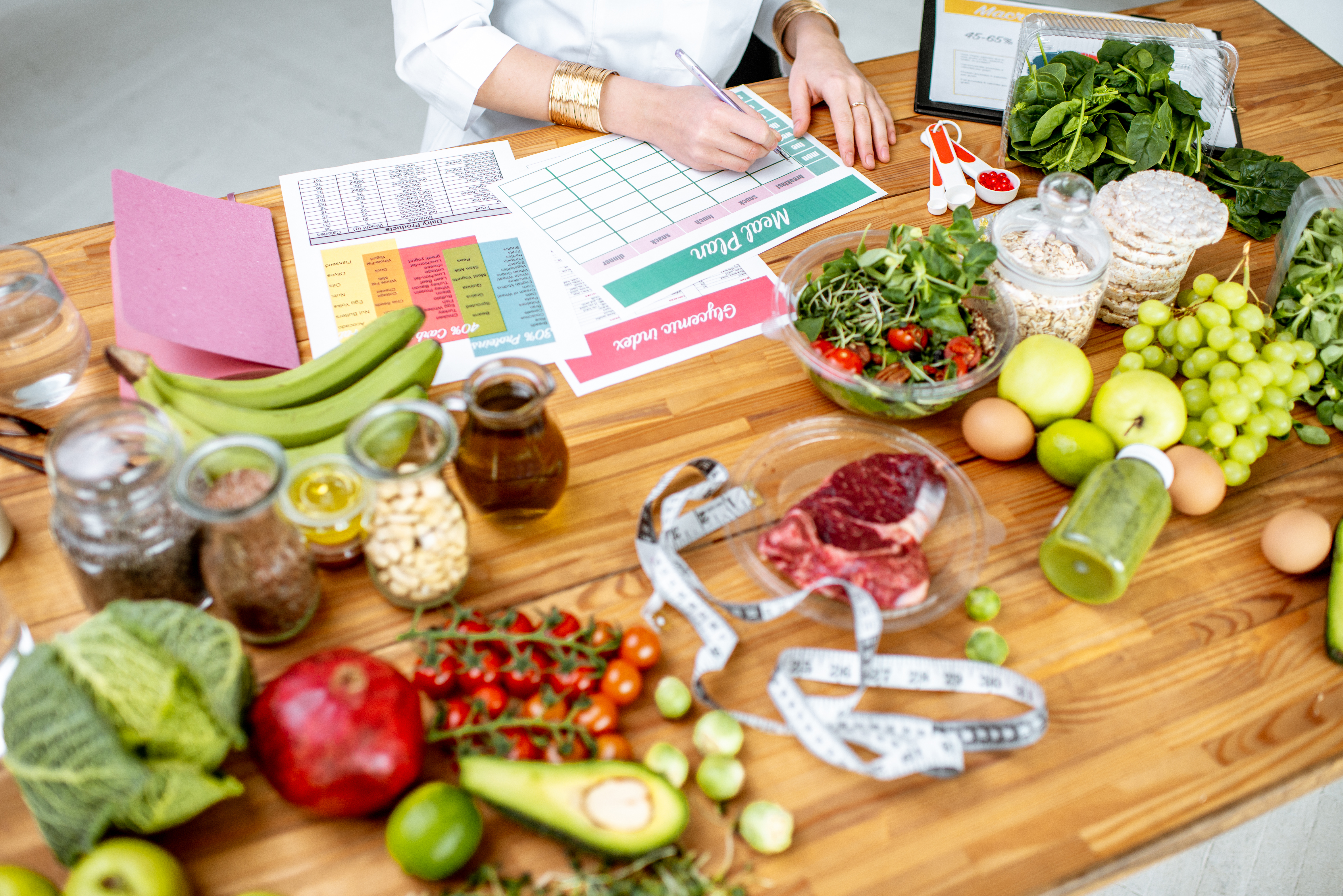 Ernährungsberaterin erstellt einen Ernährungsplan auf einem Tisch mit verschiedenen gesunden Lebensmitteln.